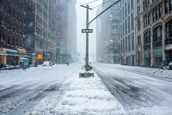A picture of a New York City street covered in snow with a "one way" sign in the middle.